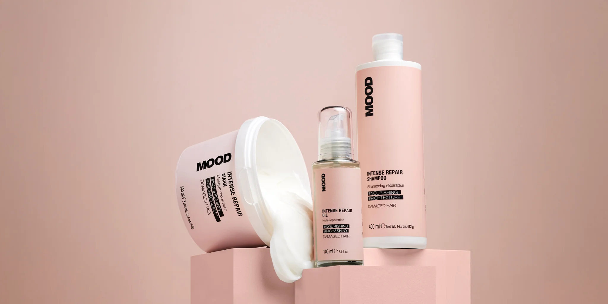 Linea_completa_MOOD_Intense_Repair_con_shampoo_Maschera_e_olio_per_capelli_danneggiati_esposti_su_piedistalli_rosa.